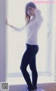 A woman in a white shirt and black leggings leaning against a window.