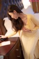 A woman in a yellow dress standing next to a bed.