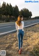 A woman standing on the side of a road with her back to the camera.