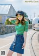 A woman wearing a green and white striped shirt and a denim skirt.