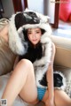 A woman in a furry hat is sitting on a couch.