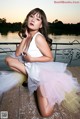 A woman in a white dress sitting on a dock.