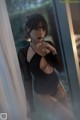 A woman in a black bodysuit leaning against a window.