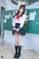 A woman in a school uniform posing in front of a blackboard.