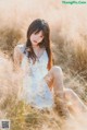 A woman in a white dress sitting in tall grass.