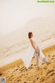 A woman walking on a sandy beach next to the ocean.