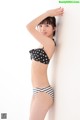 A woman in a black and white polka dot bikini leaning against a wall.