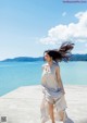 A woman in a white dress is running by the water.