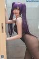 A woman with long purple hair is posing in a bathroom.