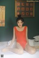 A woman in a red bodysuit sitting on a bed.