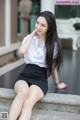 A woman in a white shirt and black skirt sitting on some steps.