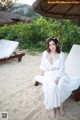 A woman in a white dress sitting on a beach.